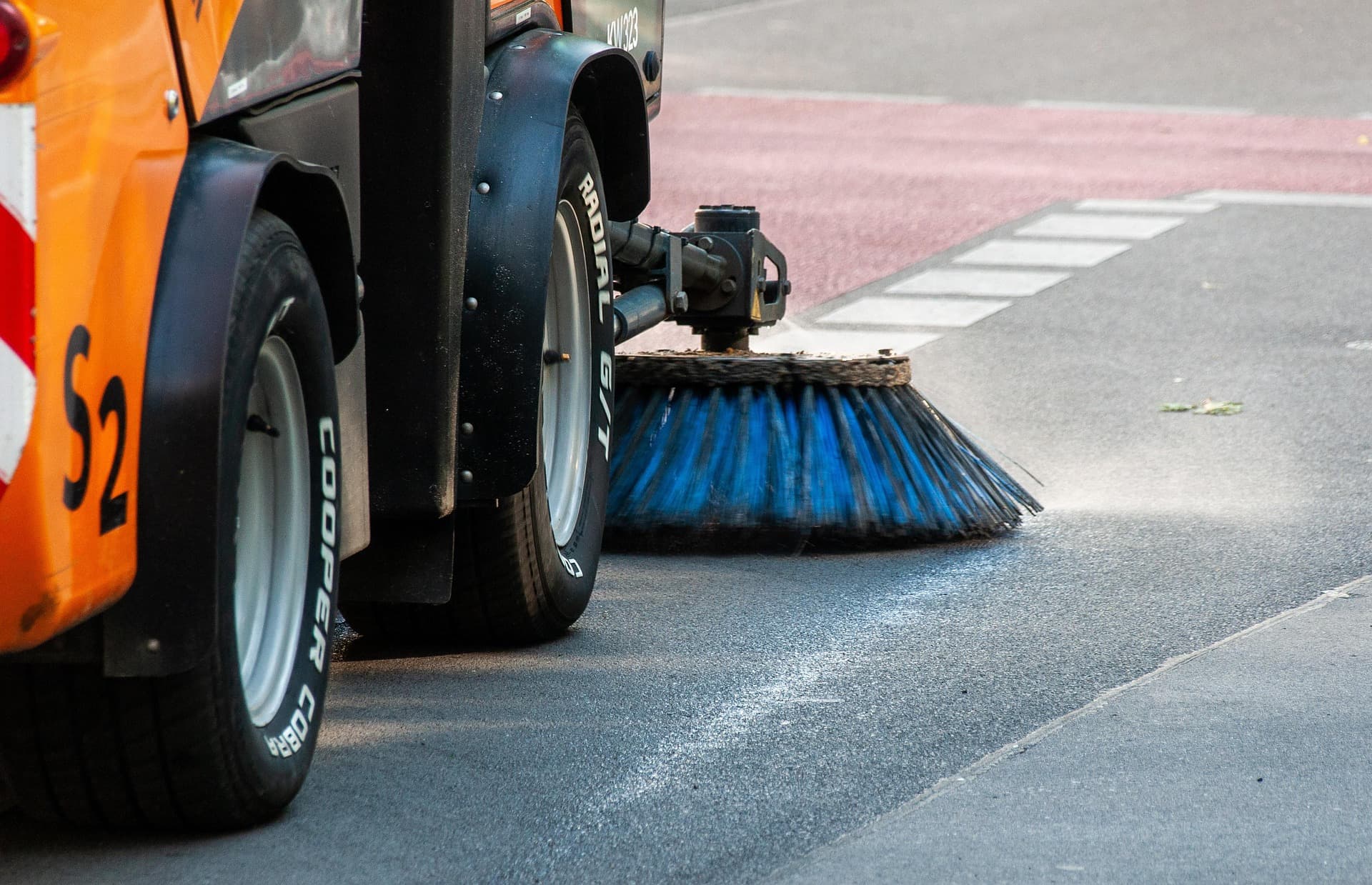 Commercial street sweeper with blue bristle brush maintaining a parking area