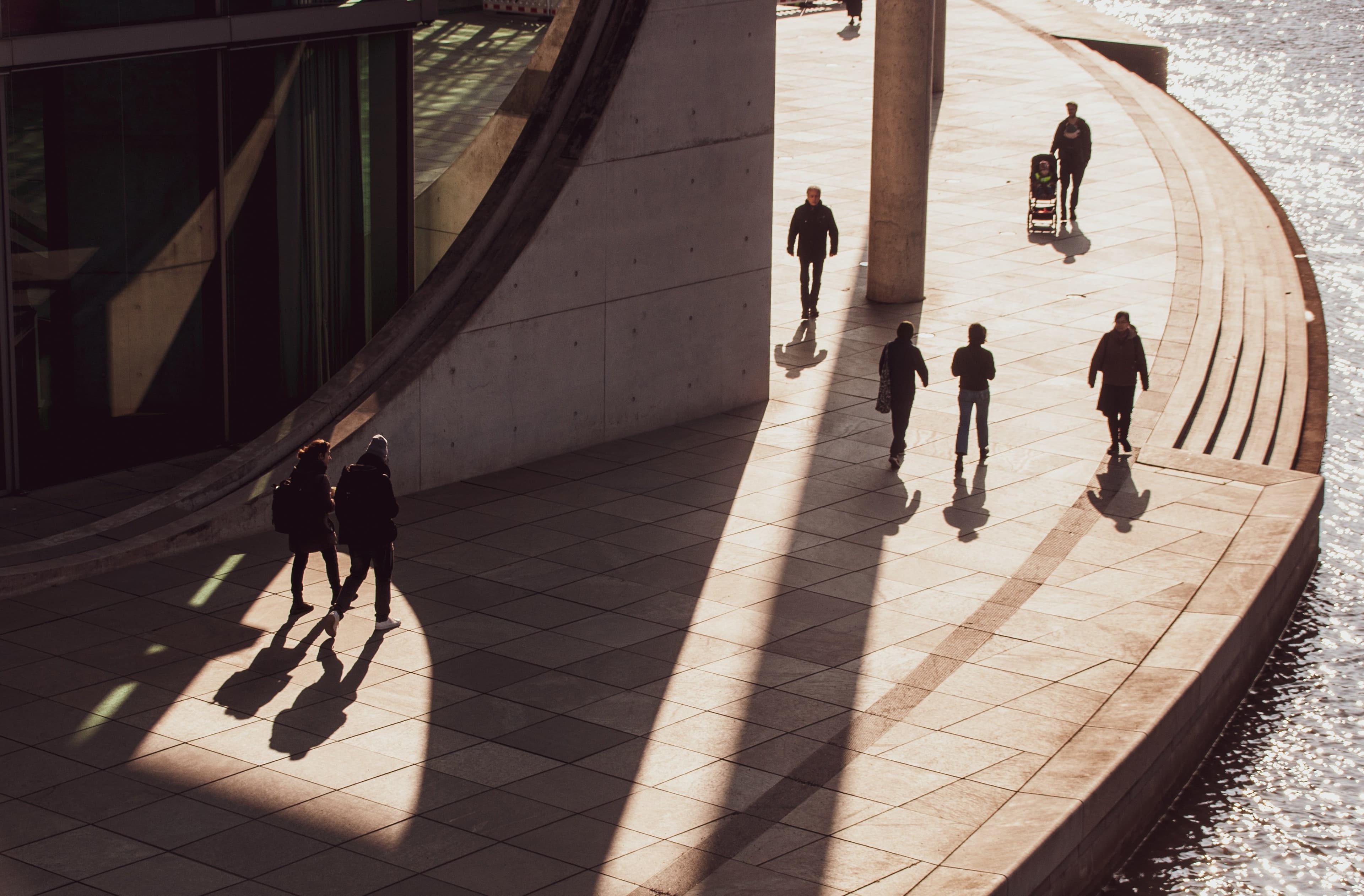 People walking across a sunlit civic plaza outside a modern government building