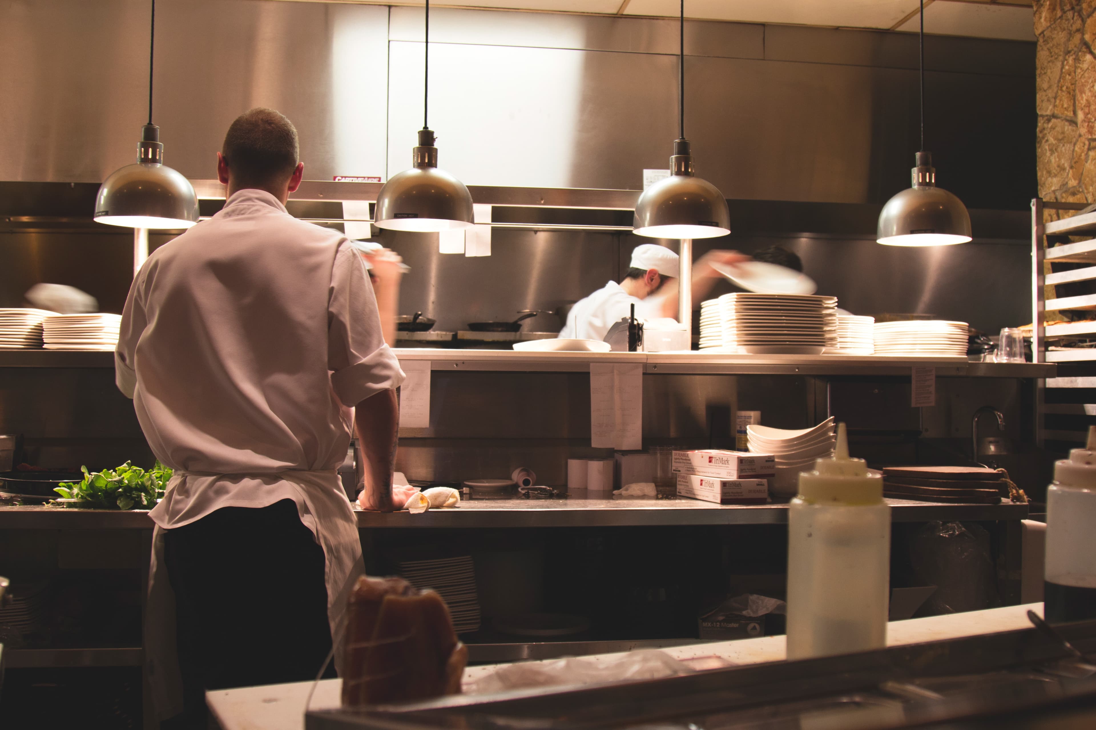 Chefs working in a busy commercial kitchen with stainless steel surfaces and pendant lights