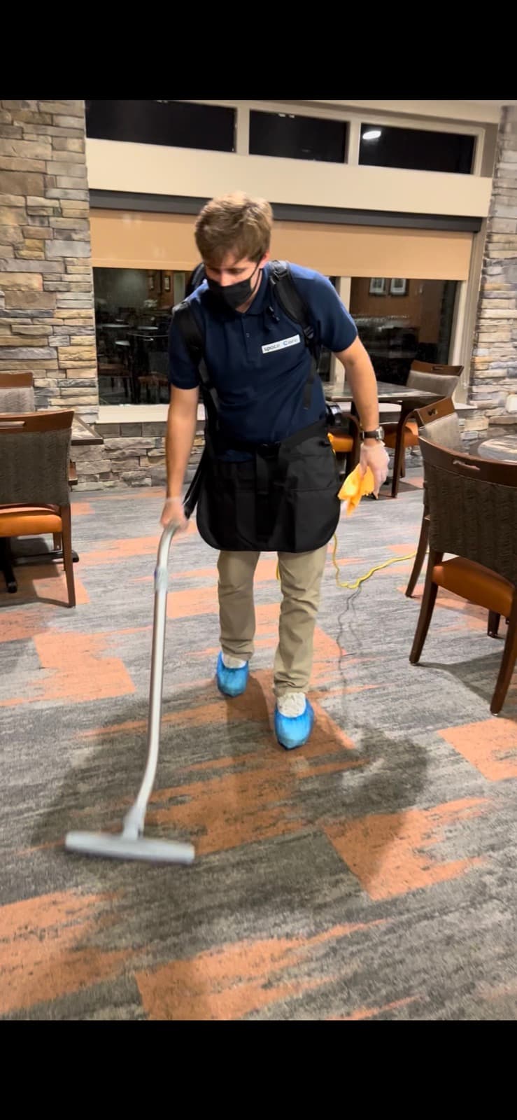 Space Care technician in branded uniform vacuuming carpet in a hospitality lobby