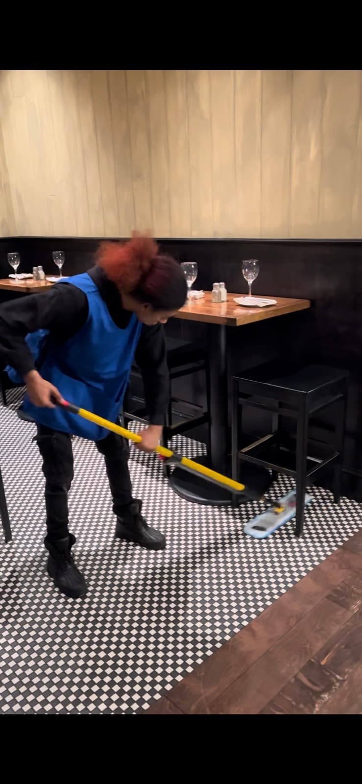 Crew member mopping a black-and-white tile restaurant floor