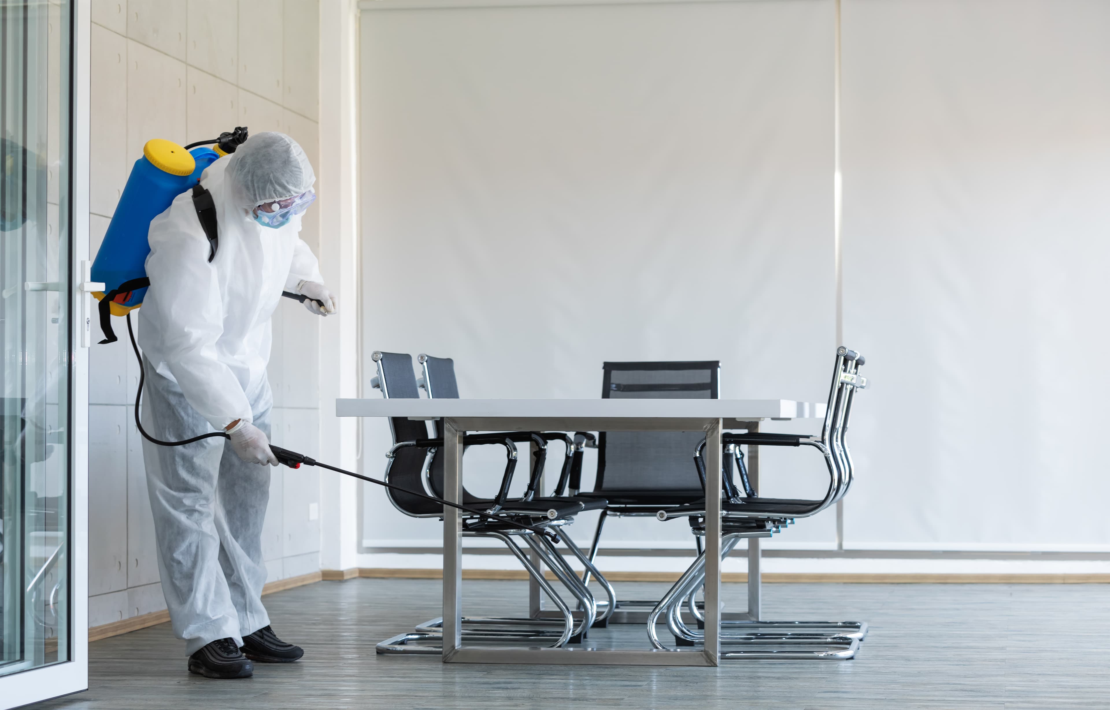 Technician in protective suit performing electrostatic disinfection spraying in an office