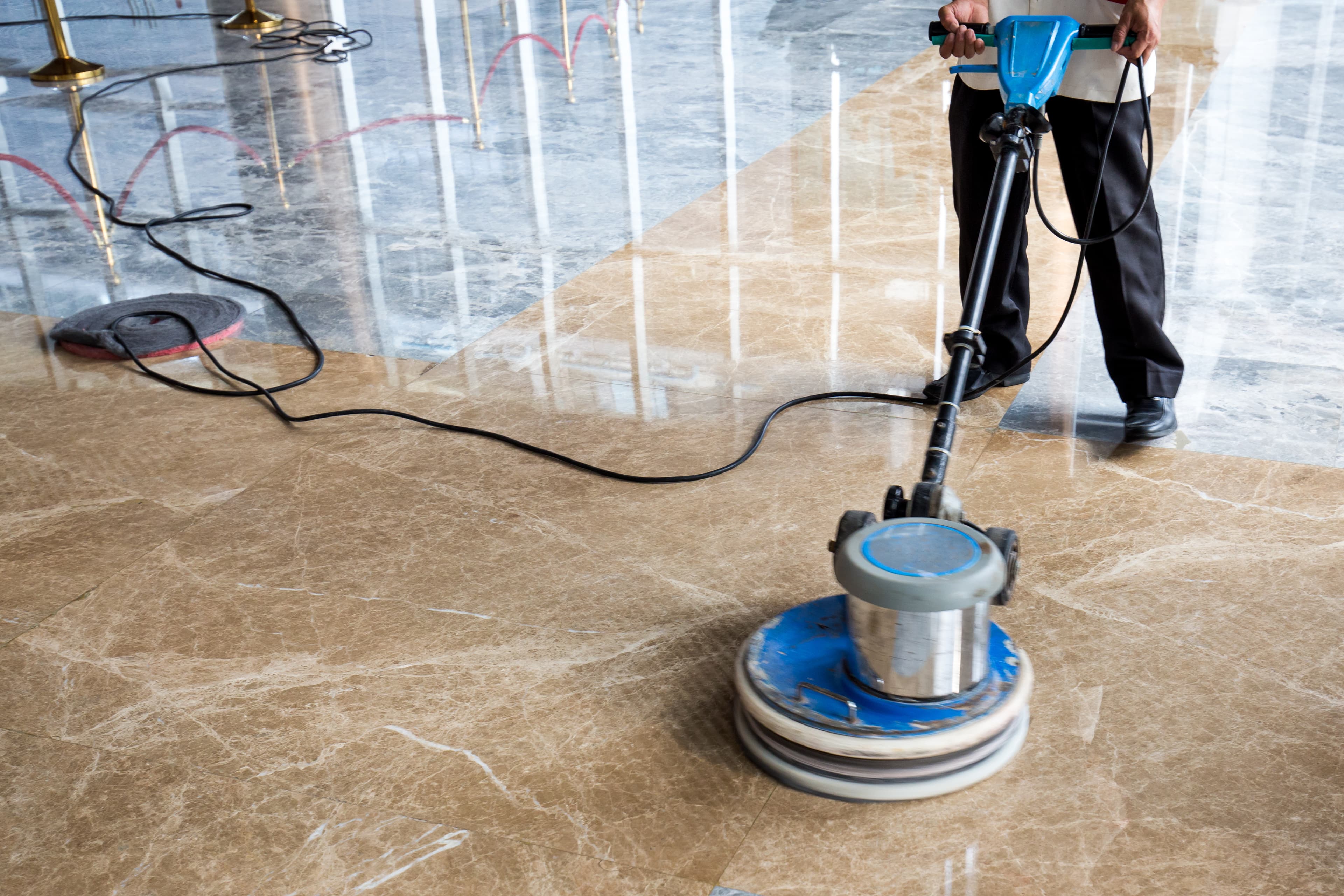 Professional floor technician polishing marble lobby floor with commercial buffer machine