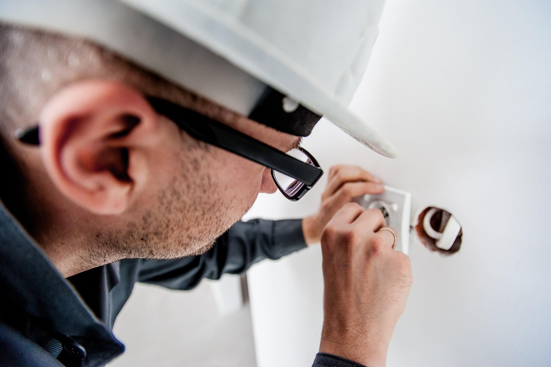 Handyman in hard hat installing an electrical outlet in a commercial building