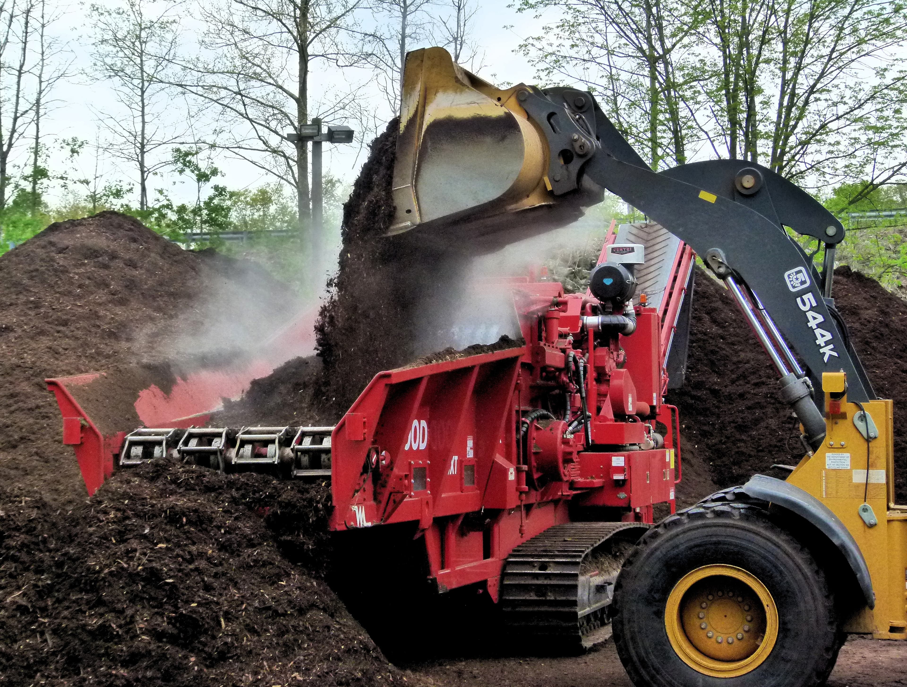 Industrial mulch grinder processing compost with front loader on a commercial landscaping site