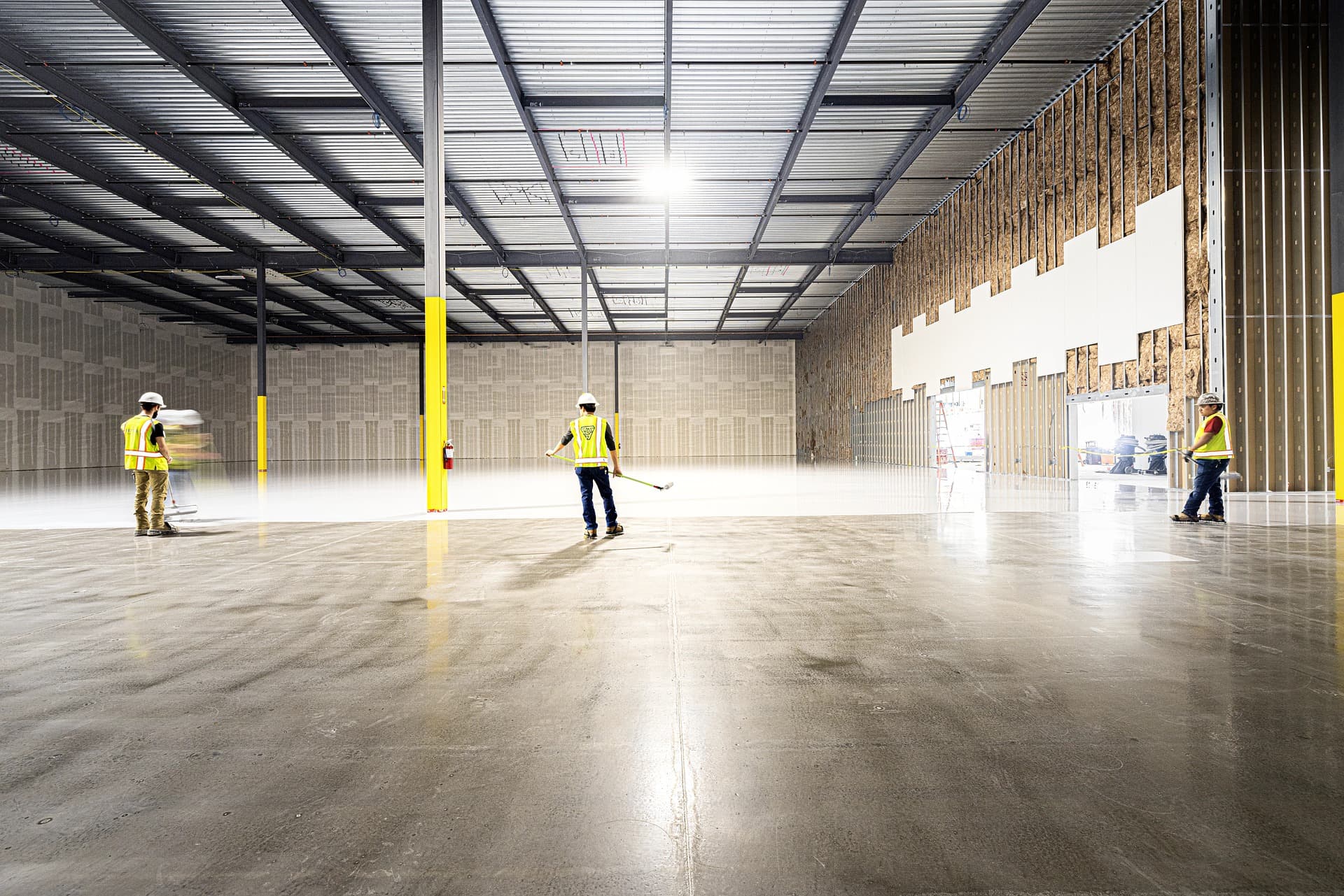 Workers in safety vests finishing a polished concrete floor in a newly constructed warehouse